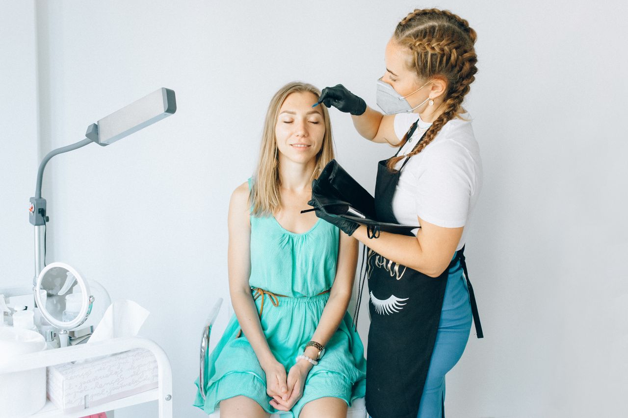 services-01 A beautician performs eyebrow microblading on a woman in a modern salon setting.