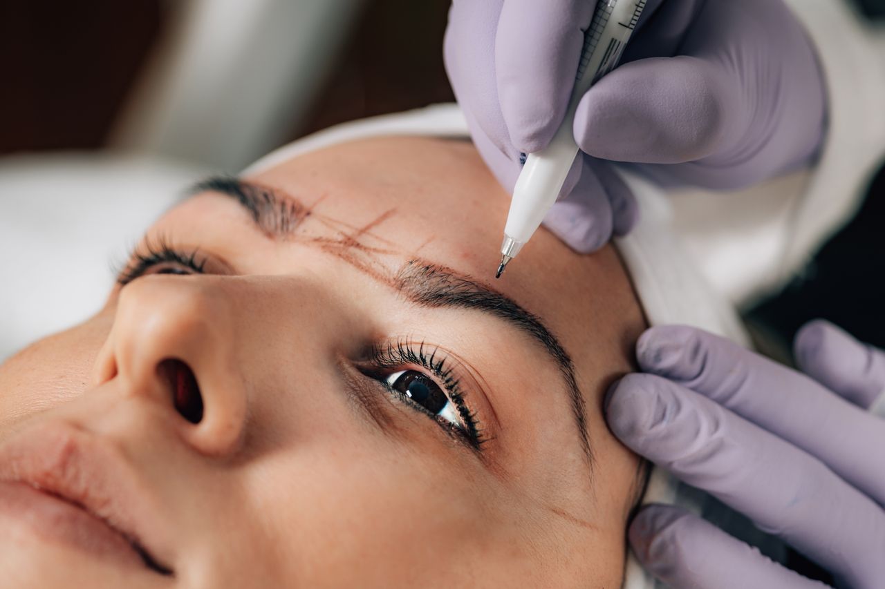 home-hero-2 A beautician performs precise microblading on a client's eyebrows in a salon.